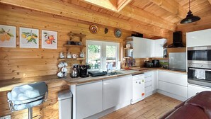 Interior de una cabaña de madera con cocina, comedor y una ventana.