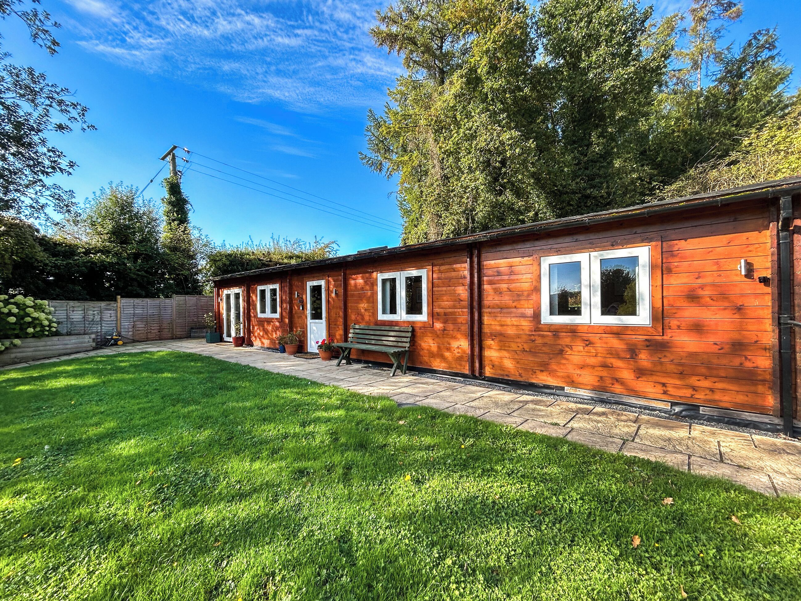 A wooden cabin with a patio, a bench, and a fenced garden area.