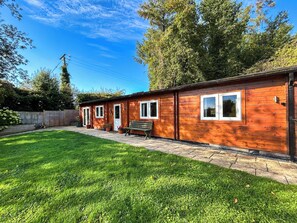 A wooden cabin with a patio, a bench, and a fenced garden area.