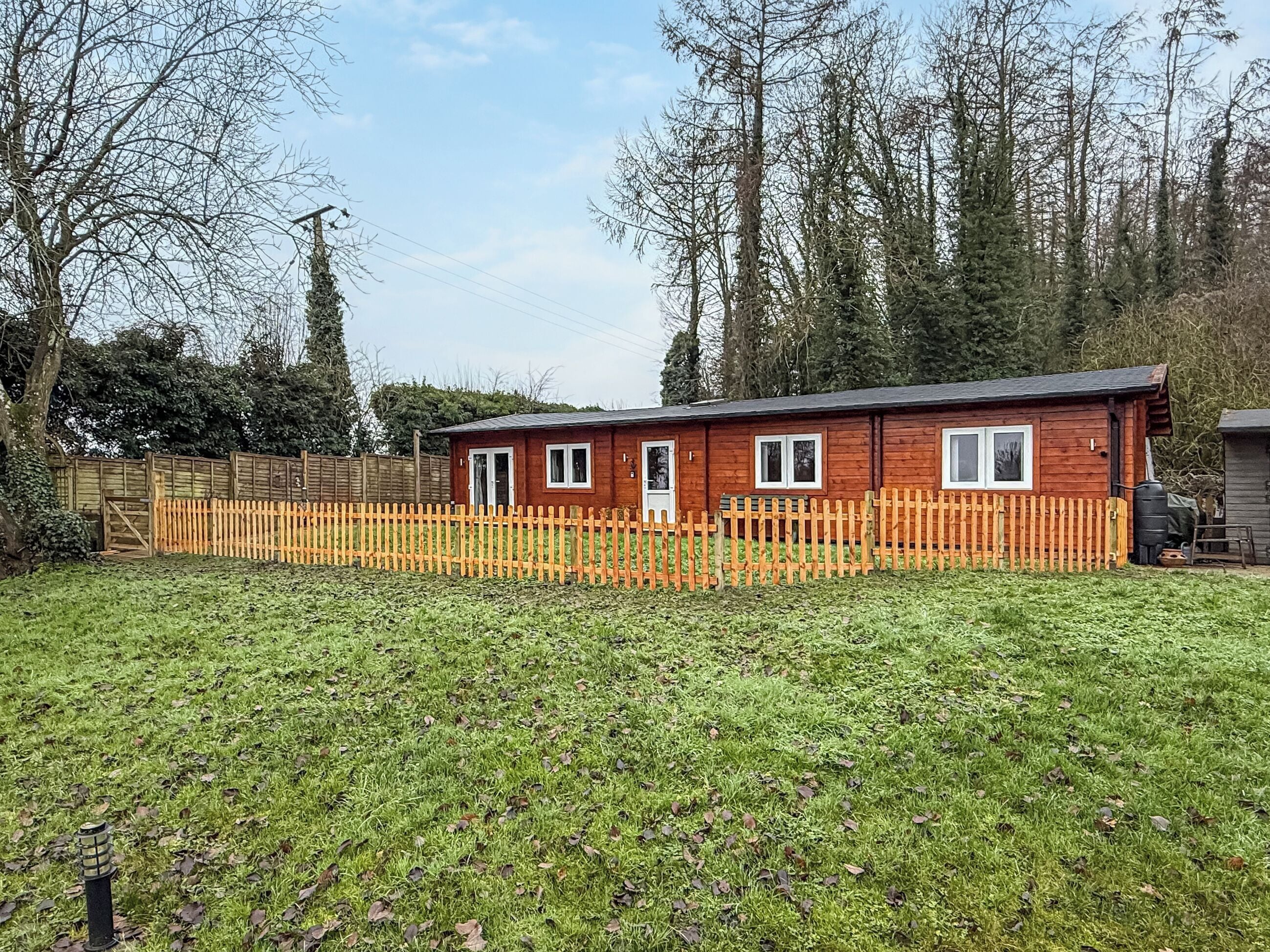 A small wooden cabin with a fenced yard, surrounded by trees.