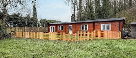 A small wooden cabin with a fenced yard, surrounded by trees.