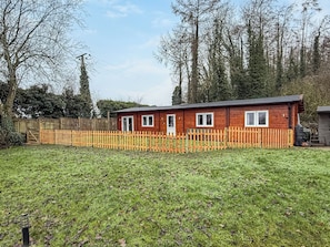Een klein houten huisje met een omheinde tuin, omringd door bomen.