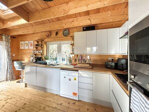 Una cocina tipo cabaña de madera con lavavajillas, armarios blancos y un ventanal grande.