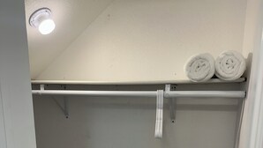 A small, white closet with a wooden floor, a ceiling light, and two rolled-up towels on a shelf. - Charming studio in delightful Salem with central heating and cooling. (Salem)