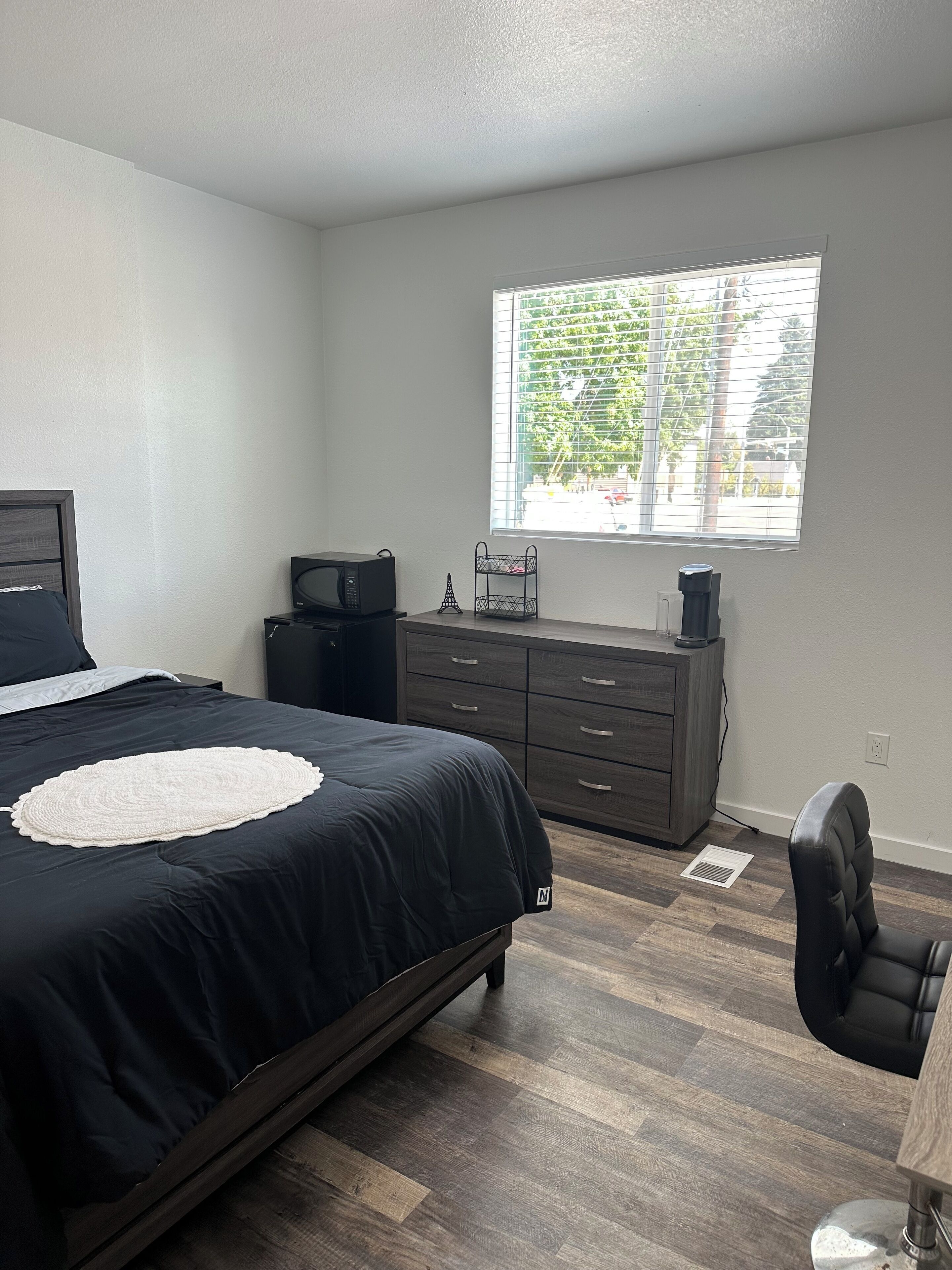 A bedroom with a bed, a dresser, a desk, and a window with blinds.