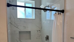 A walk-in shower with marble walls, a window, and a shower curtain. - Charming studio in delightful Salem with central heating and cooling. (Salem)