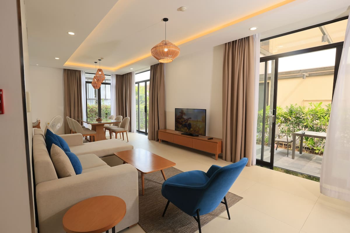 Ein modernes Wohnzimmer mit einer Couch, einem blauen Sessel, einem Couchtisch, einem Fernseher und Glastüren zum Außenbereich.