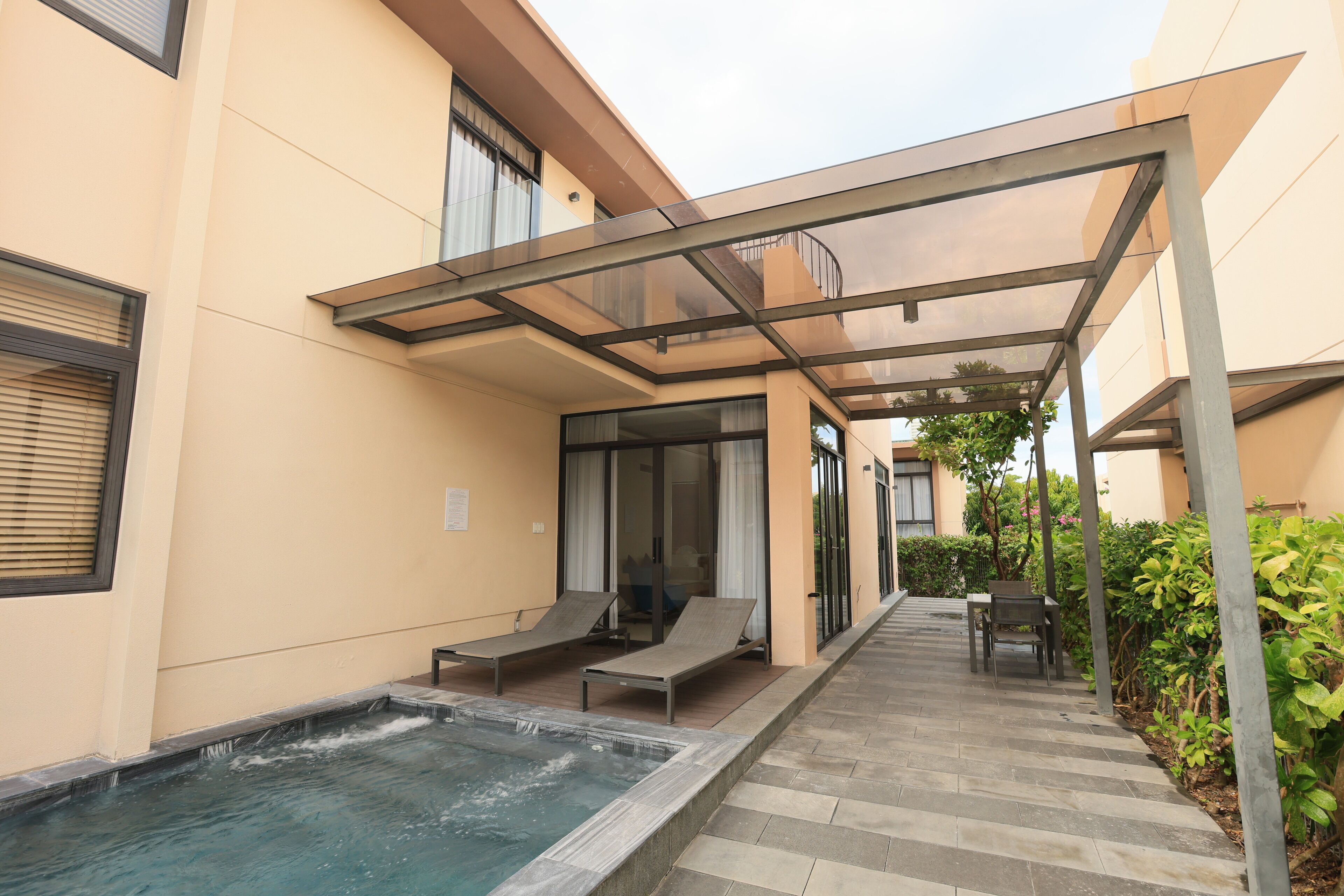 Uma área de piscina moderna ao ar livre, com um lounge envidraçado, uma banheira de hidromassagem e um espaço de estar com mesa e cadeiras.