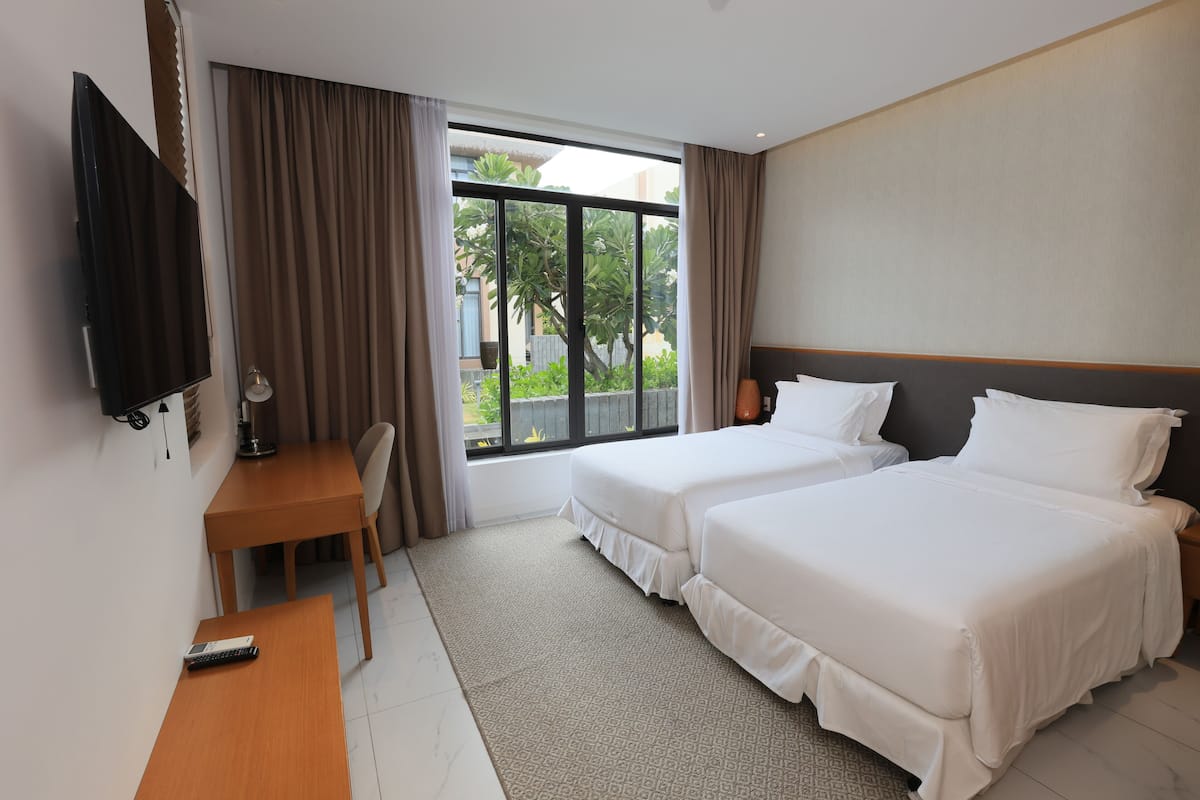 Ein Hotelzimmer mit zwei Betten, einem Schreibtisch, einem Fernseher und einem Fenster mit Vorhängen.