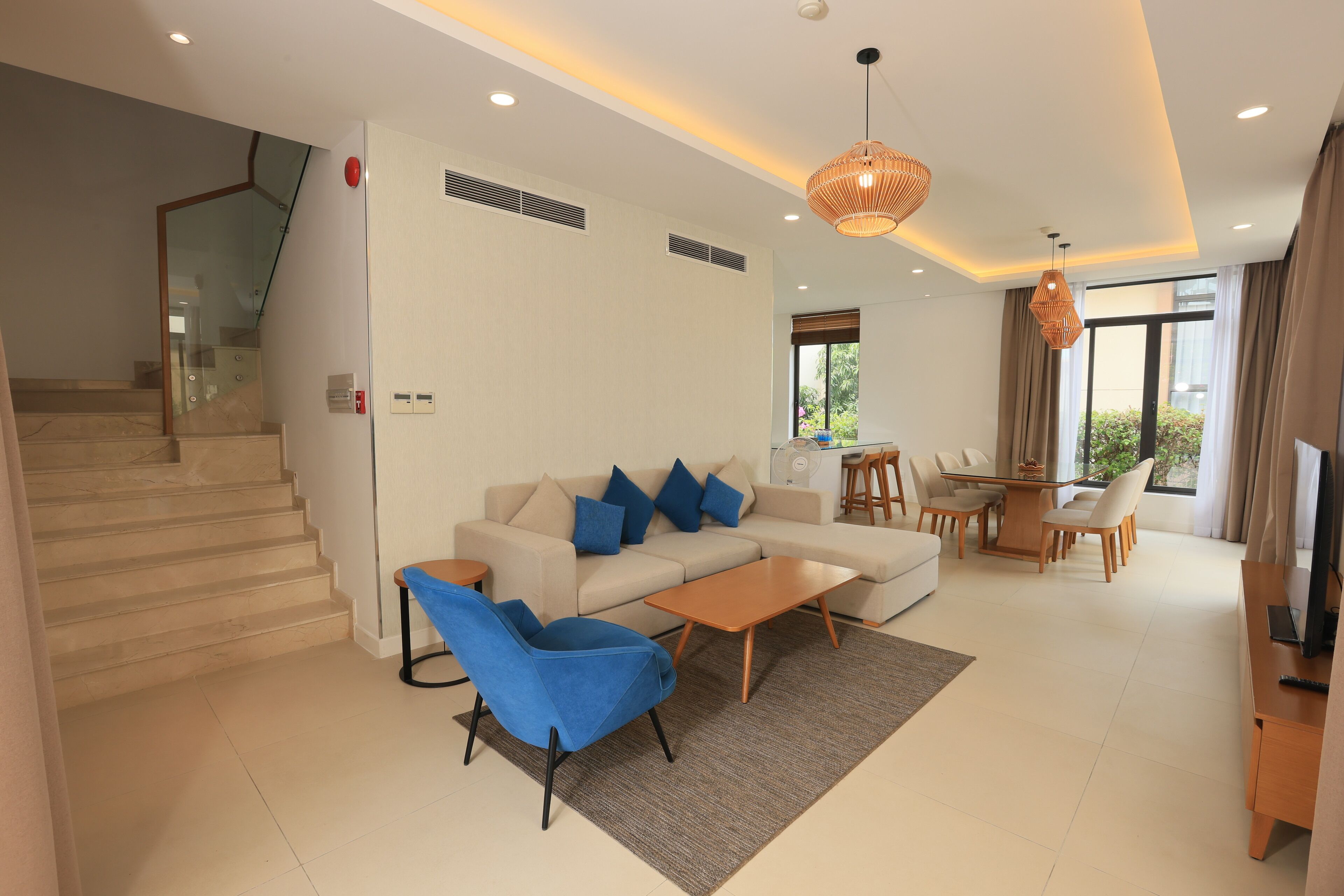 A modern living room with a sofa, blue armchairs, a coffee table, and a dining area with a table and chairs.