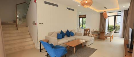 A modern living room with a sofa, blue armchairs, a coffee table, and a dining area with a table and chairs.