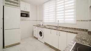 A kitchen with white cabinets, a washing machine, a microwave, and a window with blinds.
