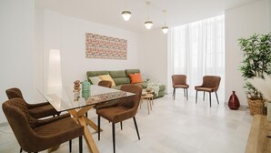 Ein modernes Wohnzimmer mit einem Glastisch, braunen Stühlen, einem grünen Sofa und einem großen Fenster mit transparenten Vorhängen.