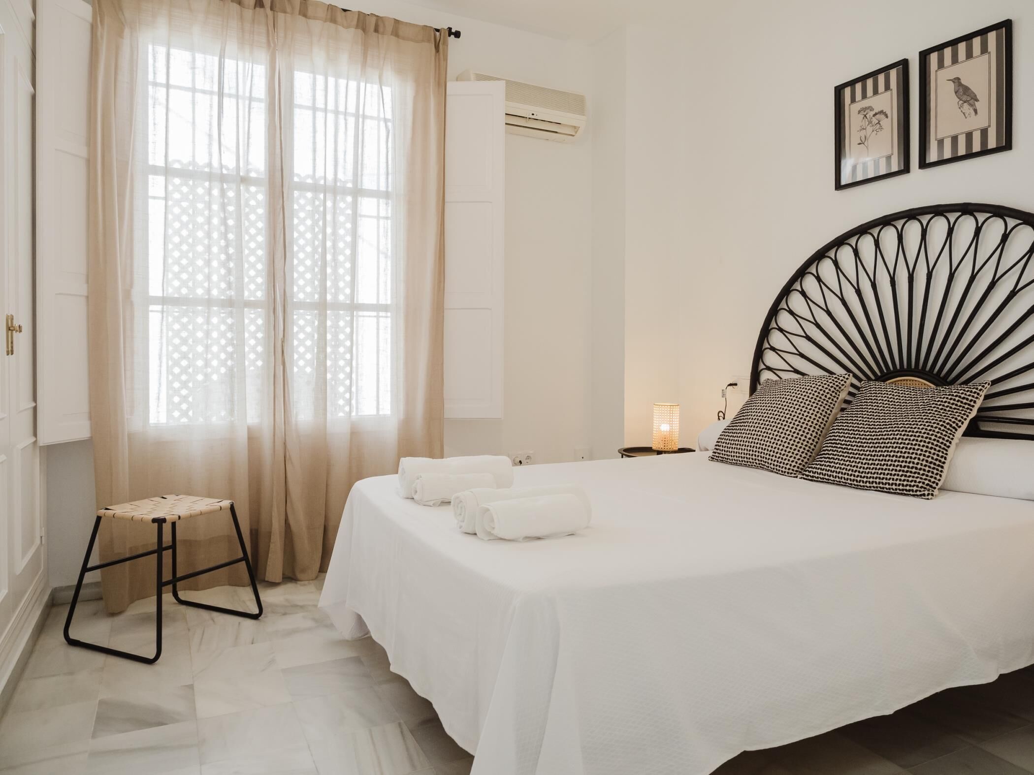 Une chambre à coucher comprenant un lit, une table de chevet, une lampe, une fenêtre avec des rideaux et des œuvres d’art murales.
