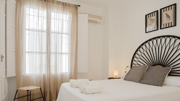 Ein Schlafzimmer mit einem Bett, einem Nachttisch, einer Lampe, einem Fenster mit Vorhängen und Wandbildern.