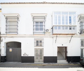 A two-story building with a white facade, a black door, and barred windows. - Sibs Sanlucar Bajamar (Sanlucar de Barrameda)