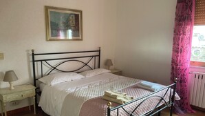 A bedroom with a bed, a nightstand, a lamp, a painting on the wall, and a window with curtains. - My home Ideal for relaxation and tranquility (Albano Laziale)