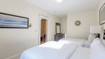 A hotel room with two beds, a door leading to a bathroom, a mirror, a clock, and a painting on the wall.