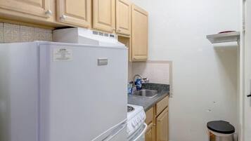 A compact kitchen with wooden cabinets, a white refrigerator, a stove, a sink, and a trash bin.