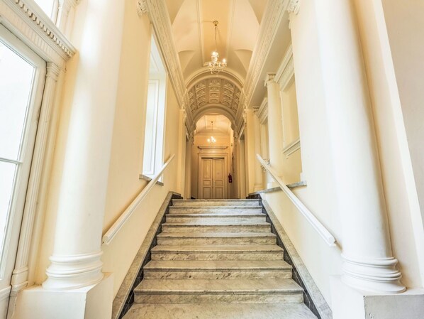 A grand staircase with marble steps and white columns, leading to a door at the end.