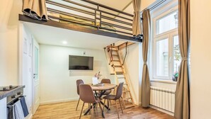 Une pièce confortable avec un lit en mezzanine, un coin repas avec une table et des chaises, un téléviseur fixé au mur et une fenêtre avec des rideaux.