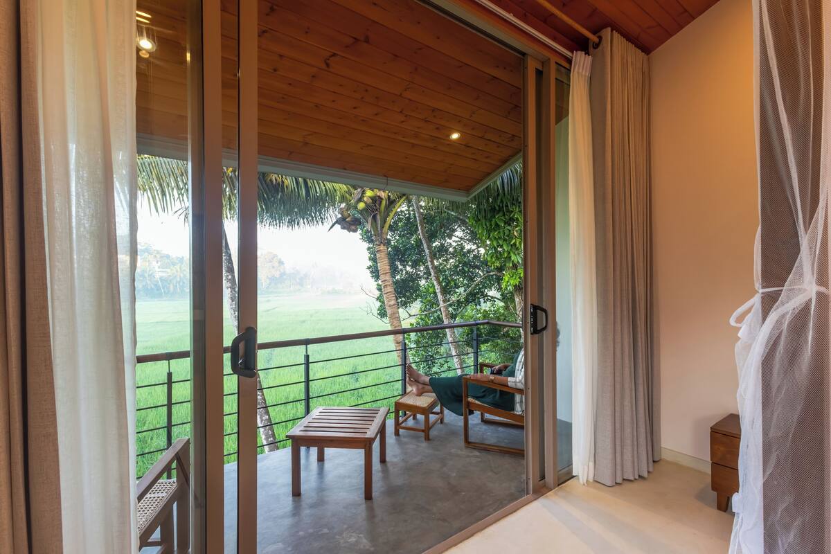 Uma varanda com vista para um campo verde, uma mesa de madeira e uma cadeira.