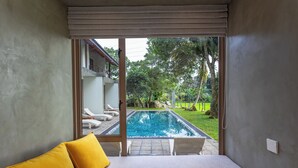 Une chambre avec vue sur une piscine, un lit avec des coussins jaunes et une porte-fenêtre coulissante.