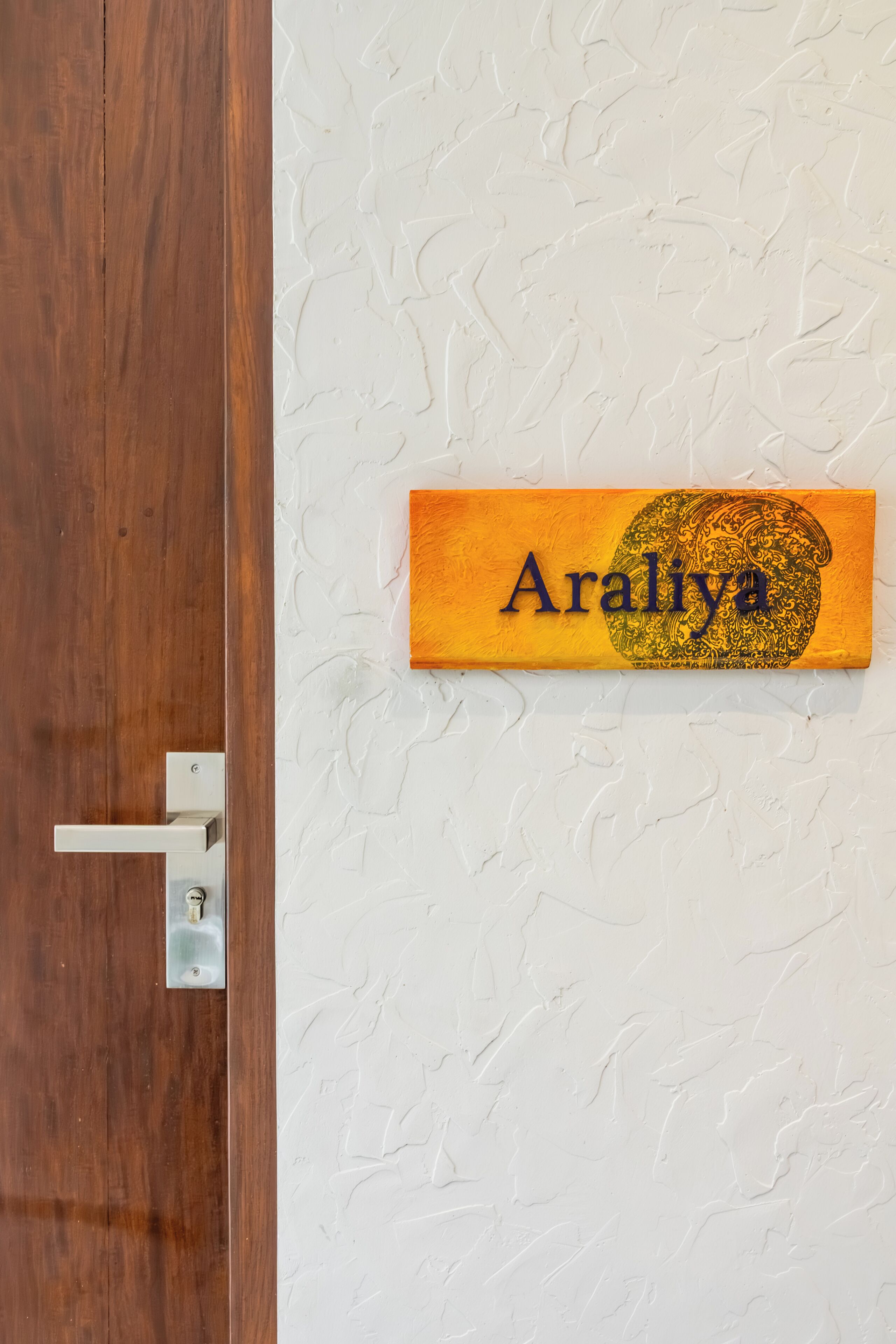 A wooden door with a metal handle and a nameplate reading 'Araliya' on a textured wall.
