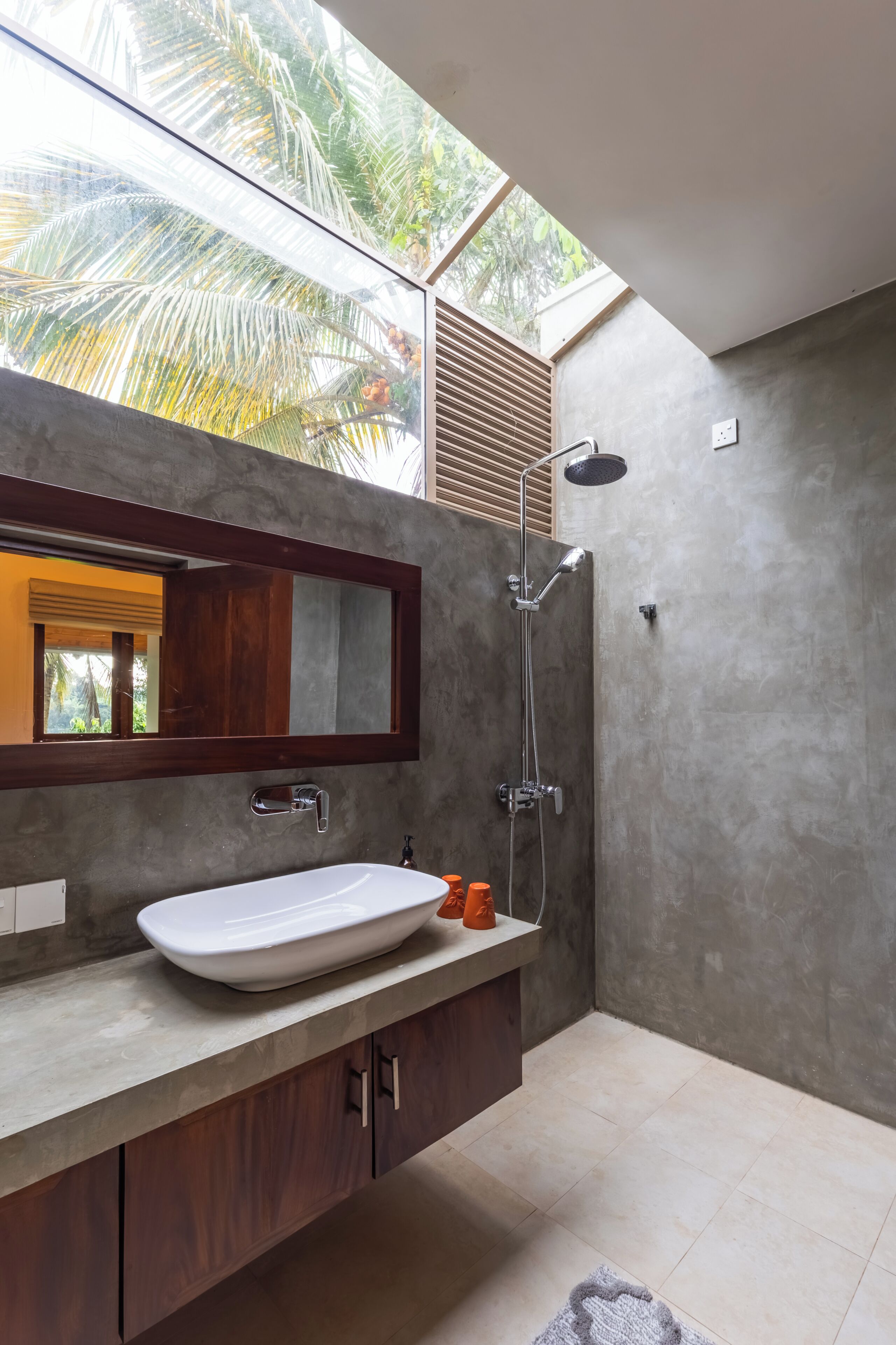 A modern bathroom with a large window, a white sink, a shower, and a wooden vanity.