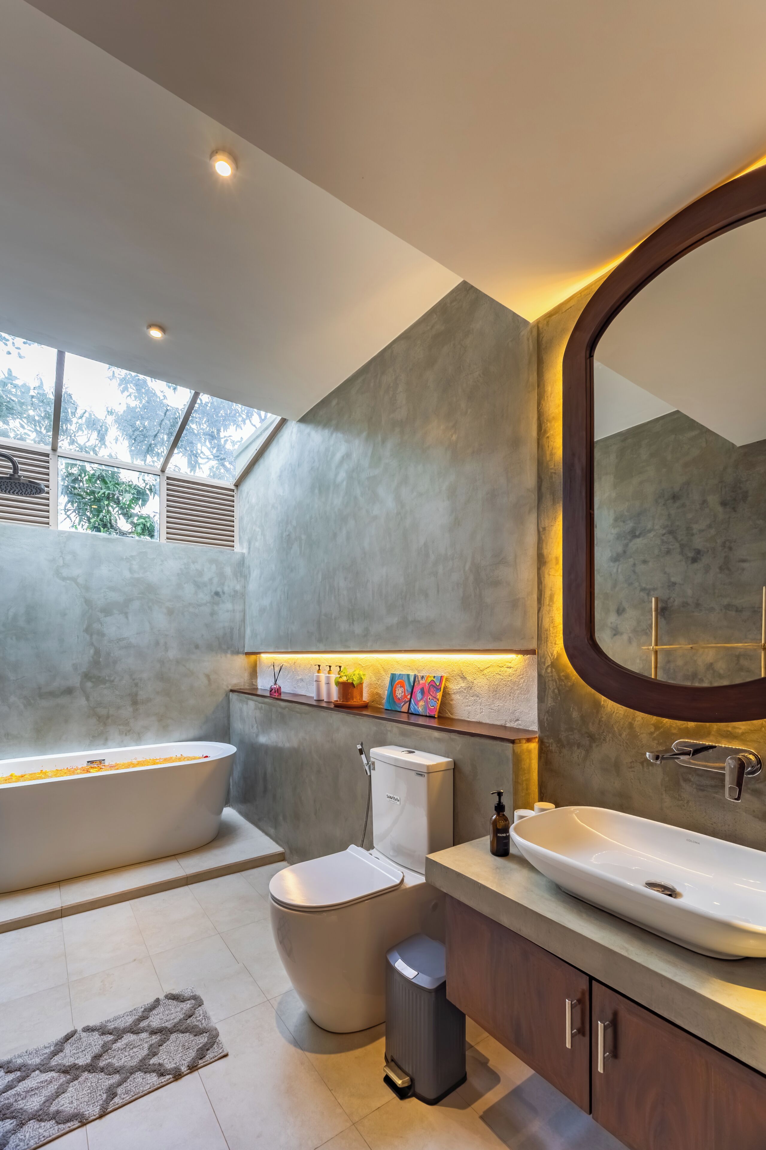 A modern bathroom with a bathtub, toilet, and sink, featuring a large mirror and a window with a view of trees.