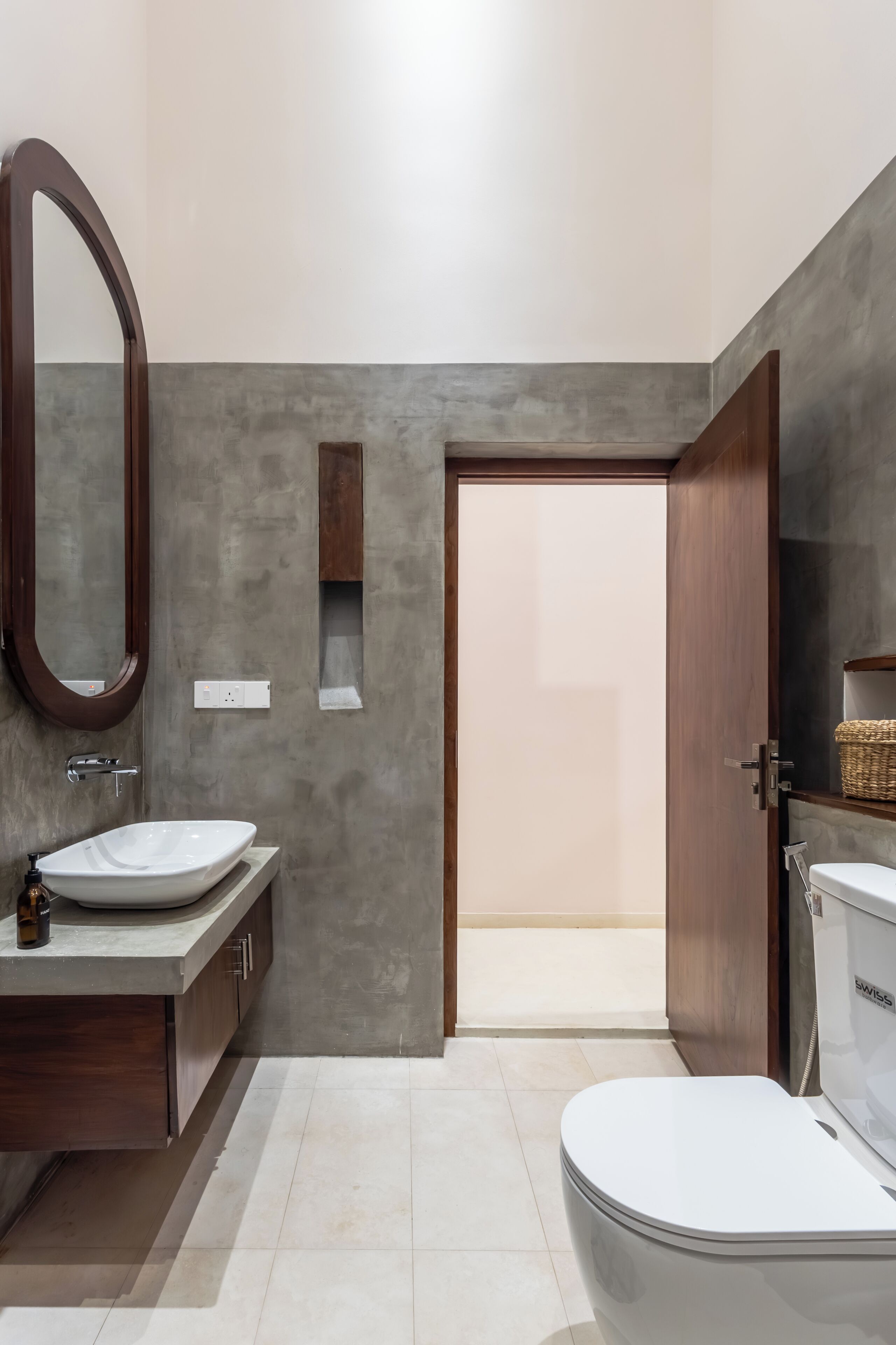 A modern bathroom with a large mirror, two sinks, a toilet, and a wooden door.