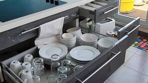 Una cocina con estufa integrada, tabla de cortar y organizador de cajones lleno de platos, tazones y vasos.
