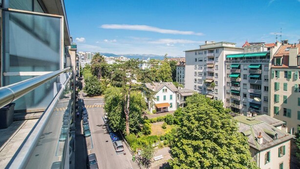 Un edificio de gran altura con varios balcones y vista a una zona residencial con árboles y viviendas.