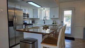 Una cocina moderna con armarios blancos, electrodomésticos de acero inoxidable, una isla de madera y un comedor con sillas blancas.