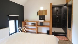Ein modernes Schlafzimmer mit einem großen Bett, einem hölzernen Schminktisch, einer Duschkabine und einem Fenster für natürliches Licht.