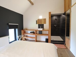 Une chambre moderne avec un grand lit, une coiffeuse en bois, une douche intégrée et une fenêtre laissant entrer la lumière naturelle.