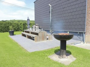 An outdoor patio with a barbecue grill, wooden furniture, and a potted plant.