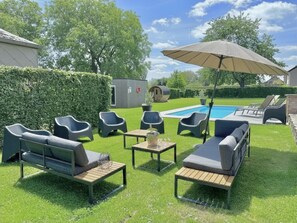 A backyard with a pool, outdoor furniture, and a large umbrella.