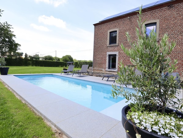 A swimming pool with lounge chairs, a brick building, and a potted plant.