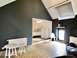 Une pièce avec un plafond en pente, un radiateur blanc, une petite table blanche, une chaise blanche, une commode blanche, un plancher en bois et une fenêtre.