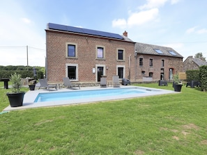 A two-story brick building with a swimming pool, outdoor seating, and solar panels.