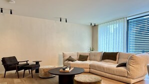 Uma sala de estar moderna com um sofá seccional bege, uma mesa de centro de madeira escura, um banquinho redondo pequeno e uma poltrona preta.