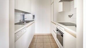 Una cocina moderna con armarios blancos, microondas integrado, un lavamanos y un horno.