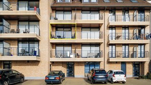 Un edificio residencial de varios pisos con balcones, un garaje y automóviles estacionados.