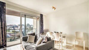 Una sala de estar moderna con un sofá gris, una mesa de comedor con sillas y un ventanal con vistas a la ciudad.