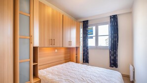 Un dormitorio con cama, armario de madera y ventana con cortinas.