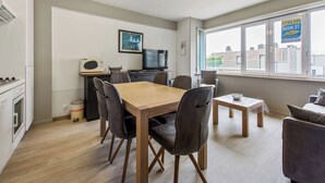 A modern kitchen with a dining area, a television, and a window with a view of buildings. - Cosy flat with central location (Koksijde)