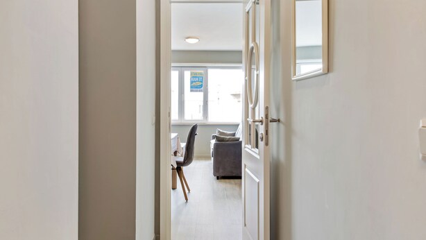 A hallway leading to a room with a window, a chair, and a table. - Cosy flat with central location (Koksijde)