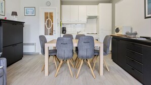 A modern kitchen with white cabinets, a wooden dining table with four chairs, and a black refrigerator. - Cosy flat with central location (Koksijde)
