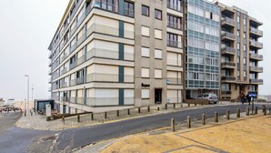 A multi-story building with balconies, a ground-level entrance, and a parking area. - Cosy flat with central location (Koksijde)